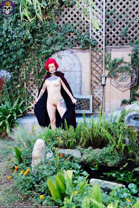 Tattooed redhead Zelda wears a cape while showing her naked body in a garden - pornpics.de