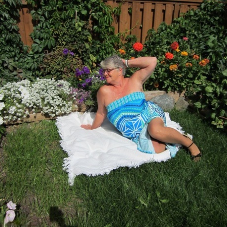 Fat nan Girdle Goddess strips to sheer pantyhose on a blanket by a flower bed