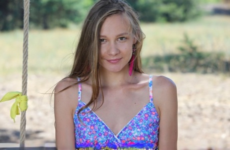 Long legged teen Mirabella doffs a dress to pose nude on a swing under a tree