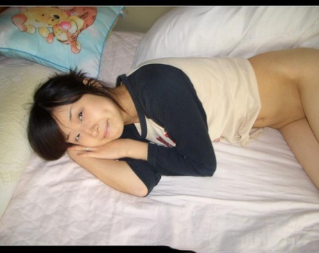Cute Asian girl showcases her bald pussy while lying naked on her bed - pornpics.de