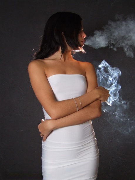 Young brunette smokes a cigarette while wrapped in tight white dress and heels