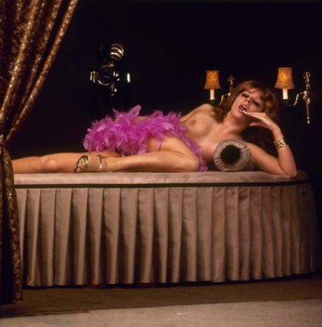 Sexy redhead strikes great nude poses on a circular bed in a feather boa