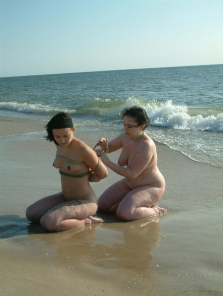 Naked girl is tied up with rope by her lesbian lover as the surf comes in