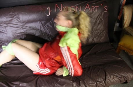 Blonde chick struggles on a futon while restrained in nylon sports clothing