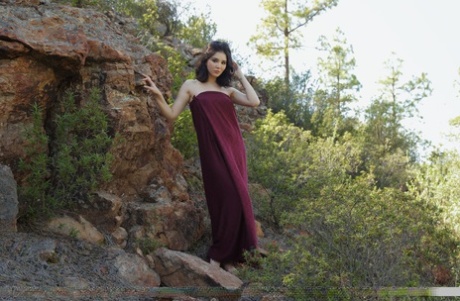 Barefoot teen Malena slips off a long dress to pose nude on a rocky bank