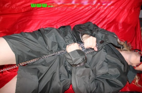 穿着尼龙雨衣和黑靴子的金发小妞用铁链束缚自己