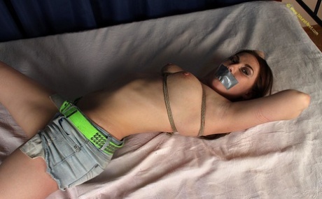Thin girl is tied to a bed while topless in shorts and silenced with duct tape