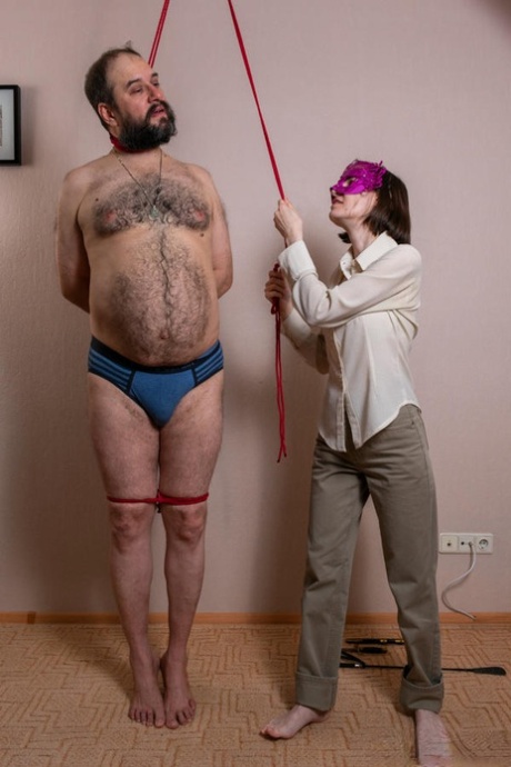 Fully clothed woman tortures a restrained man while threatening to hang him