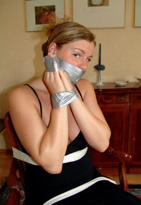 Clothed female removes duct tape from over her mouth while restrained to chair