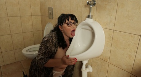 Big titted brunette Mistress Sarah licks a men's urinal while wearing glasses - pornpics.de