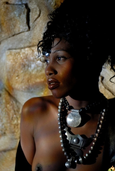 Ebony glamour model Maeva poses up against a stone wall at night