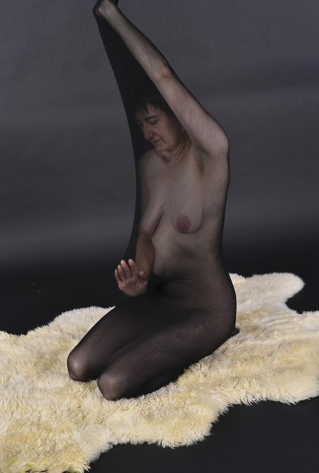 Naked mature woman encases herself in a stocking atop a rug - pornpics.de