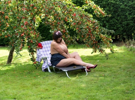 Plump amateur Roxy displays her huge boobs and bald cunt under a fruit tree - pornpics.de