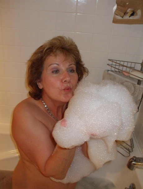 Older amateur Busty Bliss licks her lips during a playful bubble bath