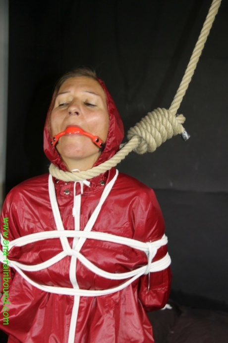 Restrained female Sandra is fitted with a ball gag and noose in a raincoat