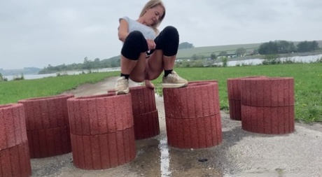 Blonde girl Juliia takes a pee atop cylinder shaped devices that block a road