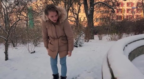 Nice girl Juliia pulls down her pants to pee on snow-covered ground in a park