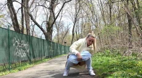 Blonde girl Bianca pulls down sweatpants to pee on a paved walking path