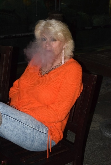 年长的金发女郎戴蒙蒂在穿着过膝长靴裸体前抽烟