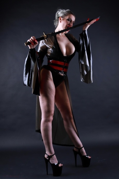 Platinum blonde solo model wields a sword while outfitted in a latex costume