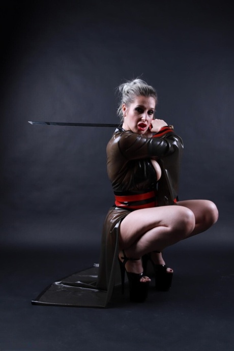 Platinum blonde solo model wields a sword while outfitted in a latex costume