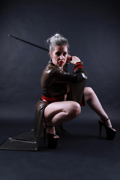 Platinum blonde solo model wields a sword while outfitted in a latex costume