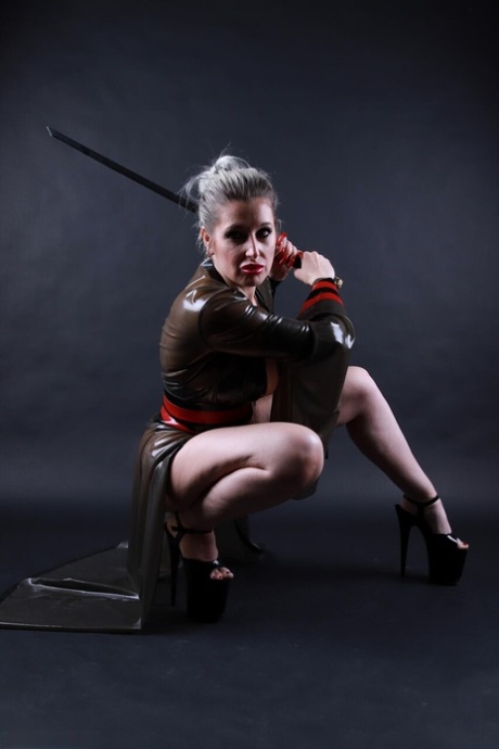 Platinum blonde solo model wields a sword while outfitted in a latex costume