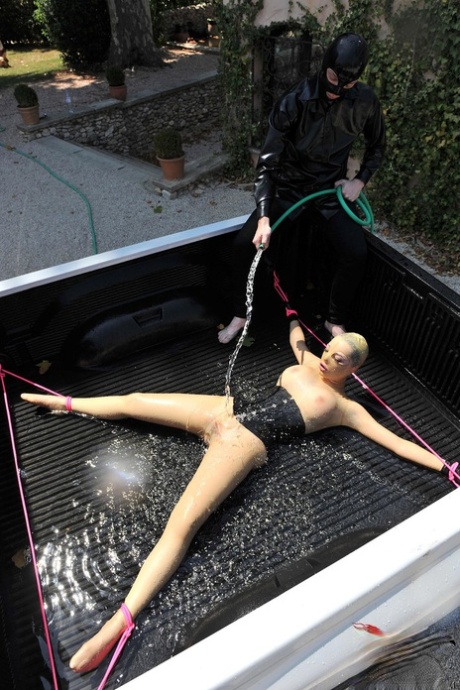 穿着乳胶的英国女孩 在 BDSM 中，乳胶露西被绑在卡车上并被喷水