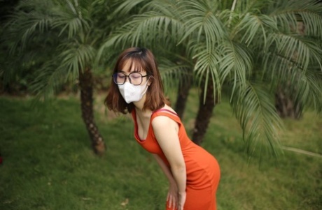 Masked Asian model with glasses posing in her tight orange dress