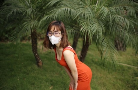 Masked Asian model with glasses posing in her tight orange dress