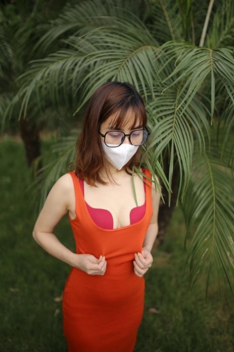 Masked Asian model with glasses posing in her tight orange dress