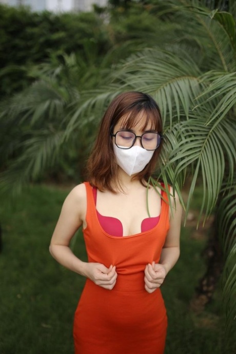 Masked Asian model with glasses posing in her tight orange dress