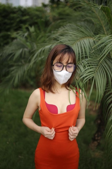 Masked Asian model with glasses posing in her tight orange dress