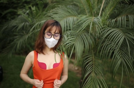 Masked Asian model with glasses posing in her tight orange dress