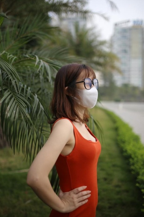 Masked Asian model with glasses posing in her tight orange dress