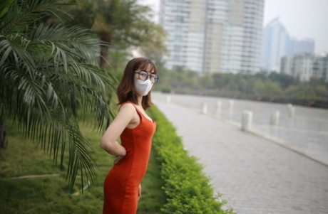 Masked Asian model with glasses posing in her tight orange dress