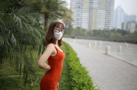 Masked Asian model with glasses posing in her tight orange dress