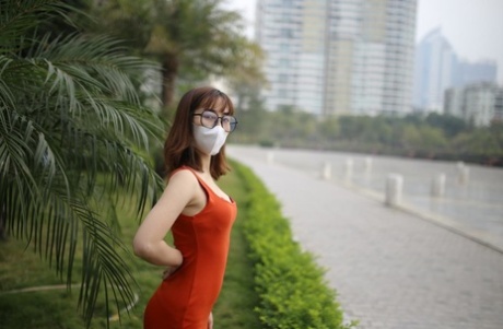 Masked Asian model with glasses posing in her tight orange dress