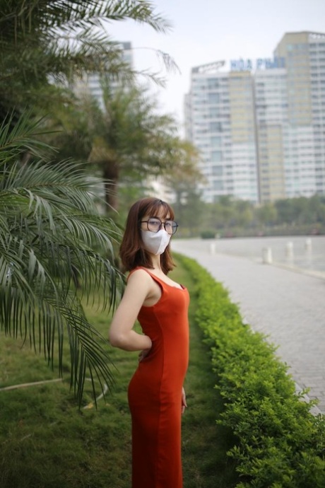 Masked Asian model with glasses posing in her tight orange dress