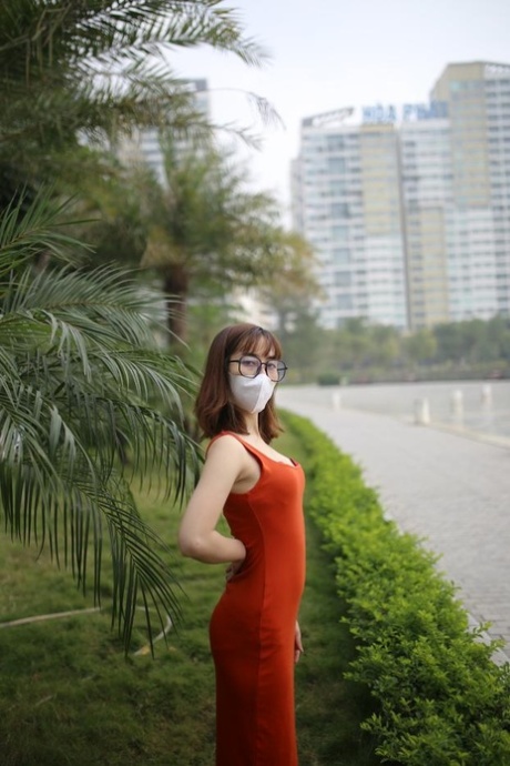 Masked Asian model with glasses posing in her tight orange dress