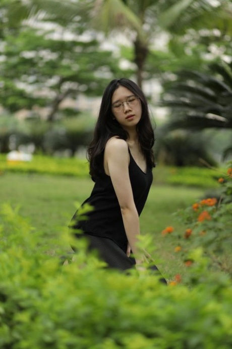 Pretty Asian girl with eyeglasses posing in her black dress at the park